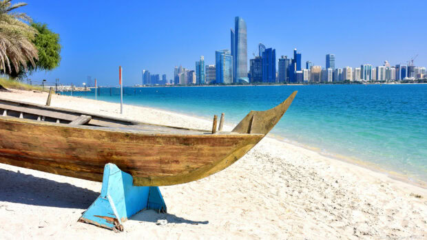 Traditional wooden boat on the beach with Abu Dhabi skyline in the background