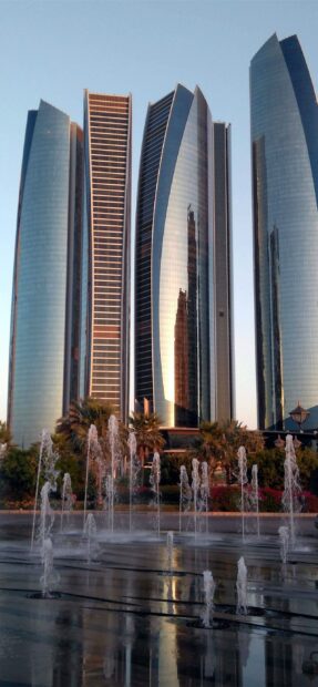Modern Abu Dhabi buildings with water fountains reflecting the cityscape at sunset