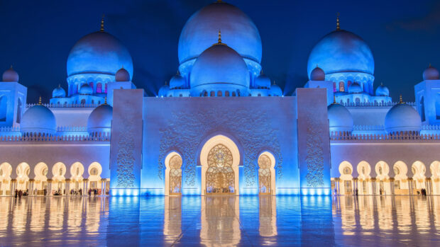The majestic mosque architecture with blue domes in Abu Dhabi at night illuminated brightly