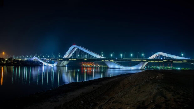 Night view of modern bridge architecture in Abu Dhabi with city lights reflecting on water