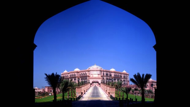 The Emirates Palace Abu Dhabi hotel framed by traditional arch with palm trees in the foreground