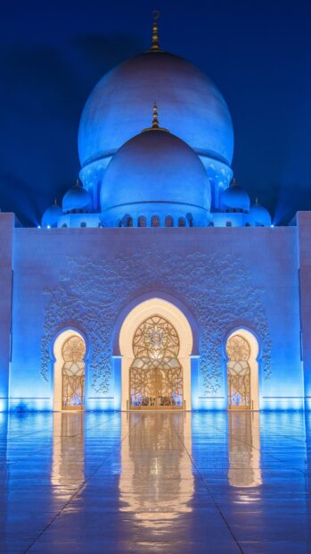 The Sheikh Zayed Mosque in Abu Dhabi under blue lighting with ornate arches and domes at night