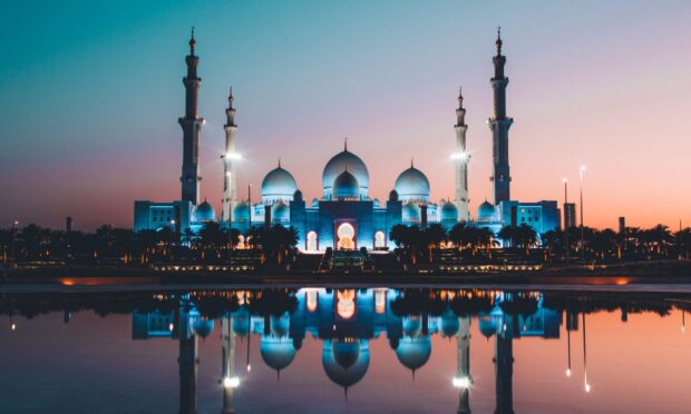 The stunning Abu Dhabi silhouette with mosque domes reflected in water at sunset