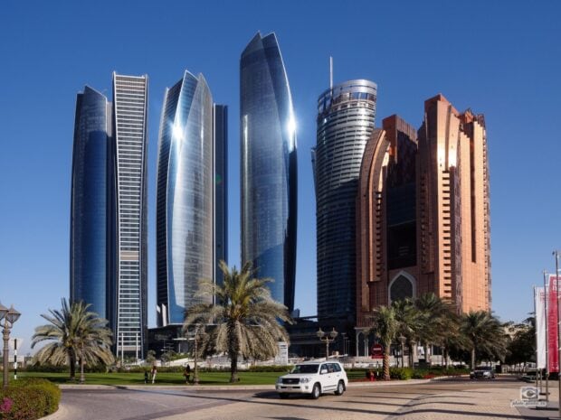 Modern Abu Dhabi skyline with palm trees and high rise buildings in clear blue sky