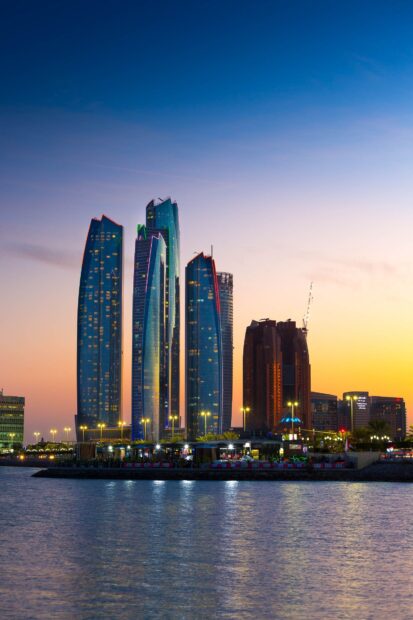 Modern skyscrapers of Abu Dhabi reflecting at sunset over the water