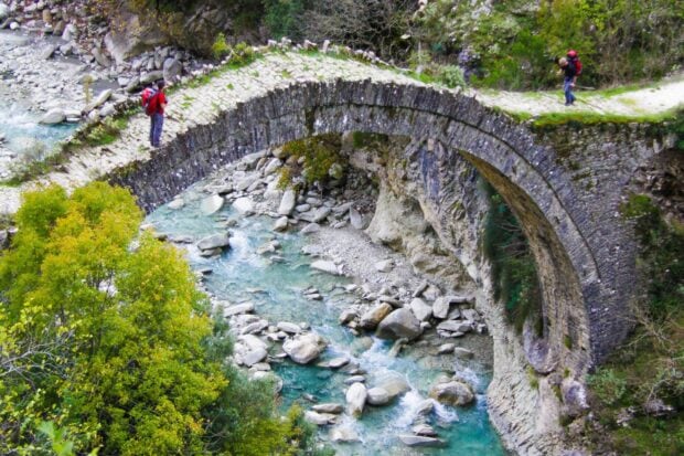 Ancient stone bridge over river with people hiking in Albania landscape