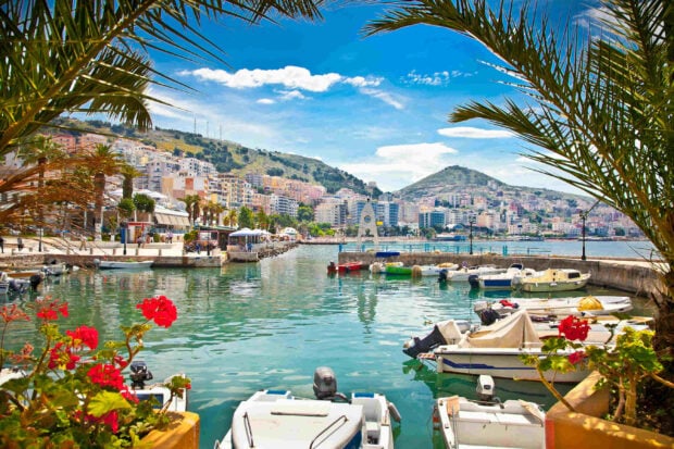 Beautiful Albania harbor scene with boats and flowers by the serene water and hillside buildings