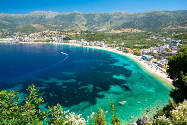 A scenic view of Albania coastline with clear turquoise waters and lush green mountains in the background