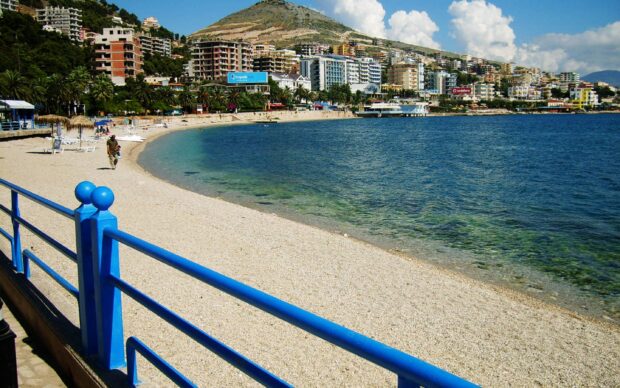 A serene beach in Albania with blue railing and clear sea water under a bright sky