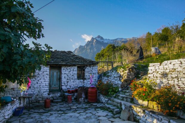 A traditional Albanian stone house with mountains in the background and colorful flowers in the garden