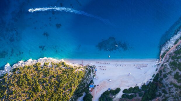 Aerial view of Albania coastline with clear blue sea and green vegetation on rocky shore