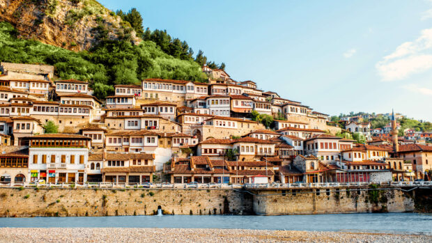 Traditional Albanian houses built on a hillside beside a river in a scenic town