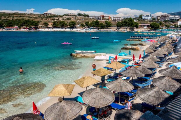 A beautiful beach scene in Albania with clear blue water and people relaxing under sun umbrellas