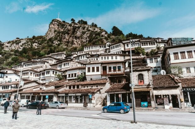 Traditional Albania architecture on hillside with parked cars and people walking