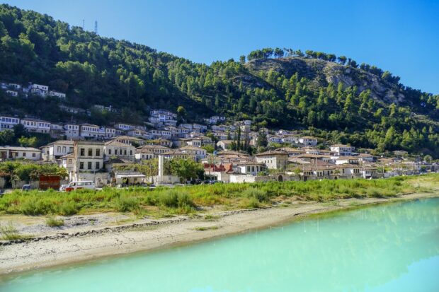 Traditional houses on a hillside in Albania with a river and green trees in the background