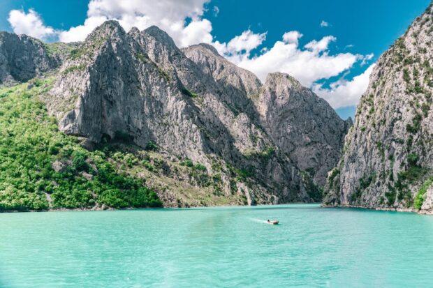 A serene lake surrounded by rocky mountains in Albania with a small boat on the water