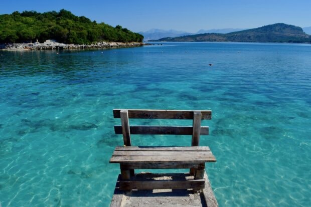 Clear turquoise water with a wooden bench on the dock in Albania