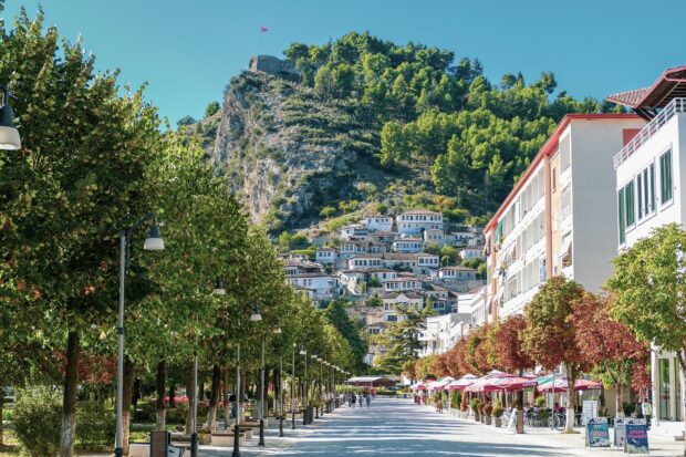 A scenic view of Berat Albania with historic houses on the hill and tree lined street