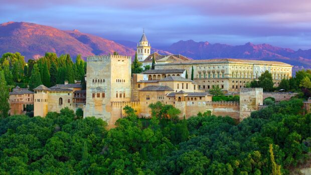 Historic Alhambra fortress surrounded by lush greenery and distant mountains at sunset