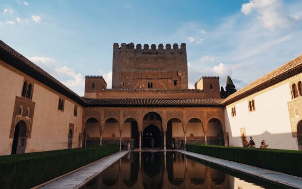 The Alhambra courtyard with detailed arches and a reflecting pool under a blue sky