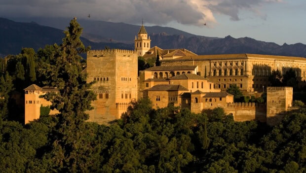 The Alhambra fortress complex surrounded by lush greenery under a cloudy sky