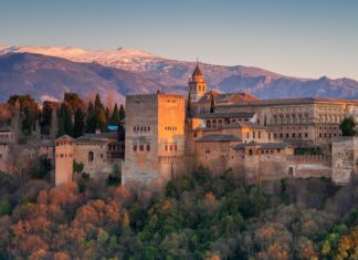Ancient Alhambra fortress surrounded by autumn trees and mountains at sunset