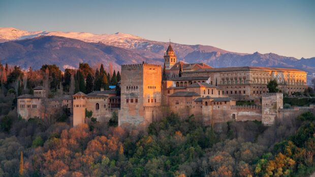 Ancient Alhambra fortress surrounded by autumn trees and mountains at sunset