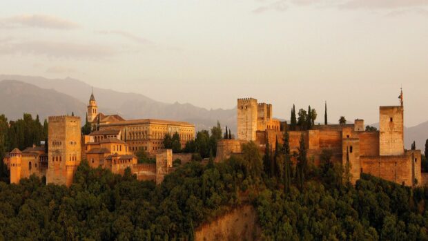 Historic Alhambra fortress surrounded by lush greenery and mountains at sunset