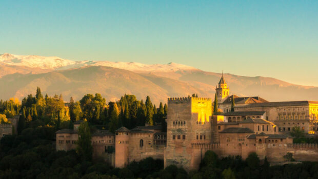 The historic Alhambra palace surrounded by lush trees with snow capped mountains in the background