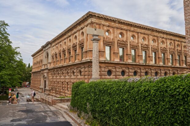 Historic Alhambra architecture with detailed stone carvings and green hedges in the foreground