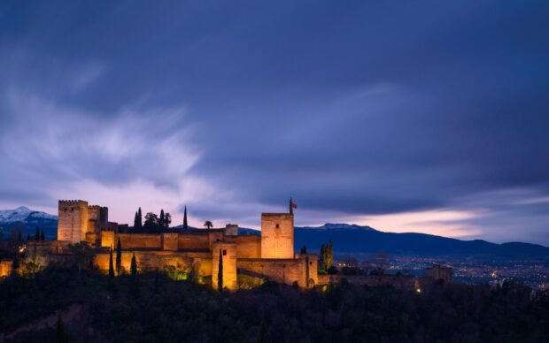 The Alhambra fortress illuminated at dusk with mountains in the background