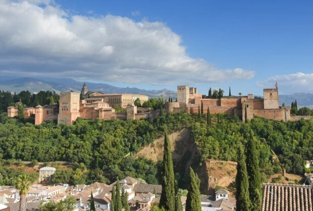 The historic Alhambra surrounded by lush greenery and mountains under a clear blue sky