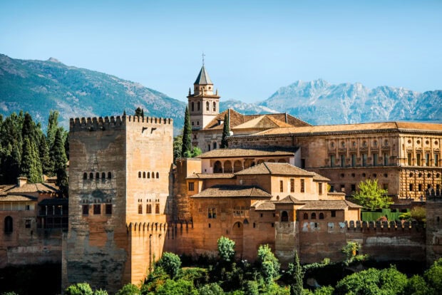 Historic structure of Alhambra surrounded by trees and mountains in bright daylight