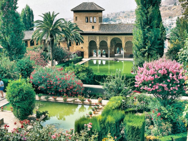 A vibrant Alhambra garden with lush greenery and blooming flowers surrounding a historic building