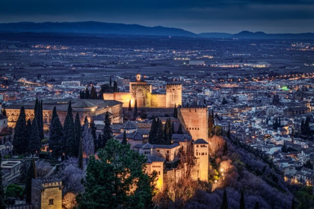 The Alhambra fortress illuminated at dusk with city lights in the background