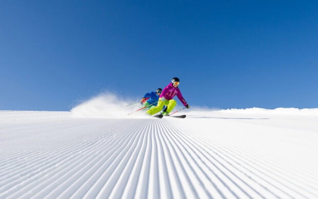 Two athletes skiing alpine on a fresh snow slope under clear blue sky