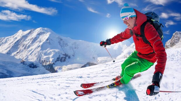 A skier wearing colorful gear skiing down a snowy alpine slope on a bright sunny day