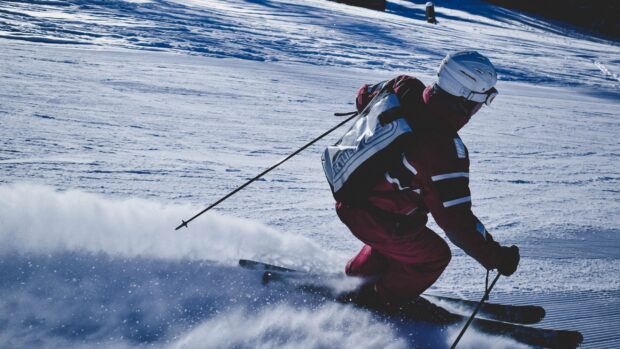 A skier wearing a helmet and jacket skiing downhill on fresh snow in alpine skiing