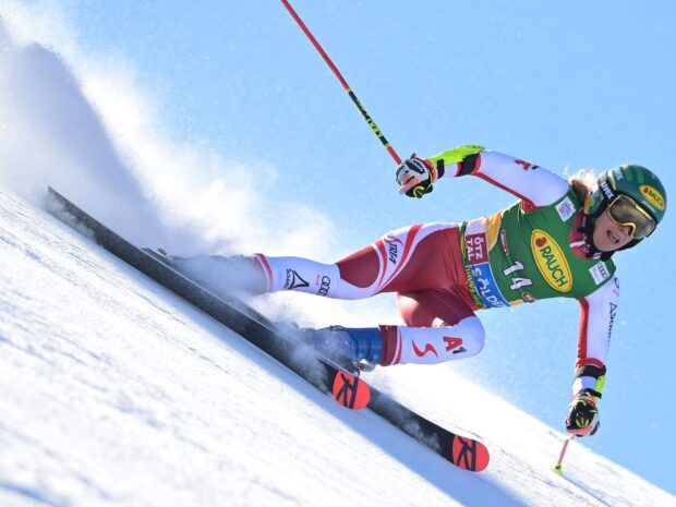 Female alpine skiing competitor racing downhill with red and white suit on snowy slope