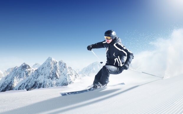 A skier is enjoying alpine skiing on a snowy slope with mountains in the background