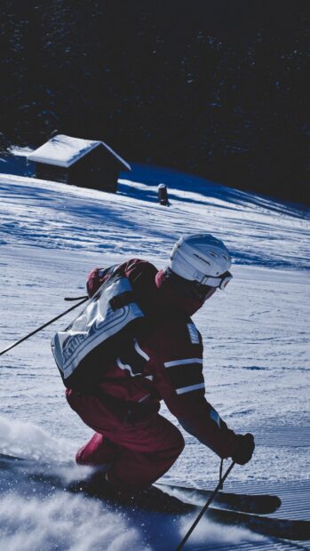 A skier wearing protective gear skiing down a snowy alpine slope