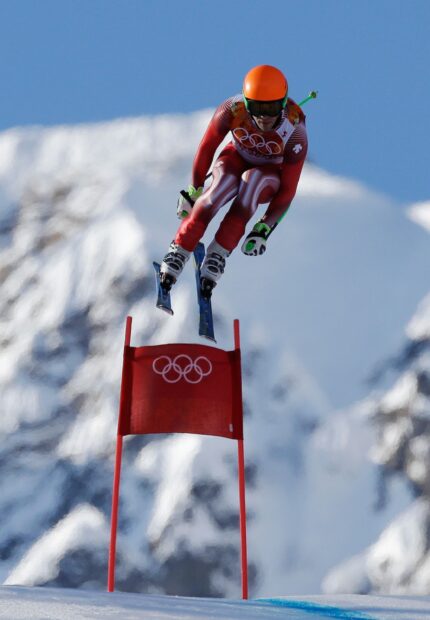 A skier in red gear performing alpine skiing at high speed on a snowy mountain slope