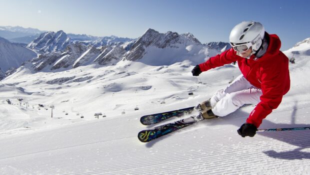 A skier wearing red jacket practicing alpine skiing on groomed snow slopes