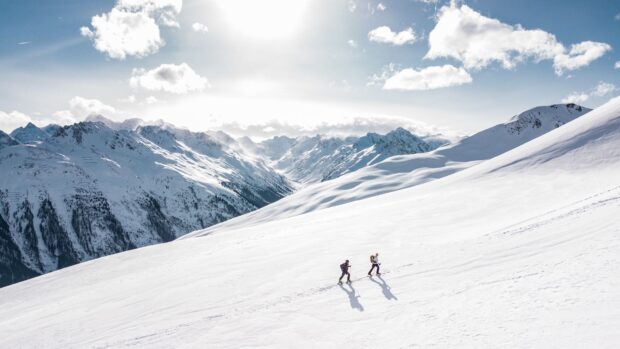 Two alpine skiing hikers ascending a snowy mountain slope under a bright sky