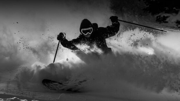 A skier in alpine skiing gears carving through deep snow powder on a mountain slope