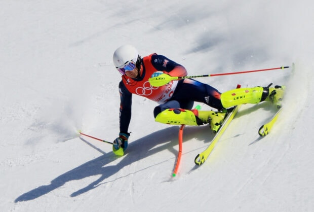 A skier competes in alpine skiing wearing bright yellow gear and a white helmet on a snowy slope