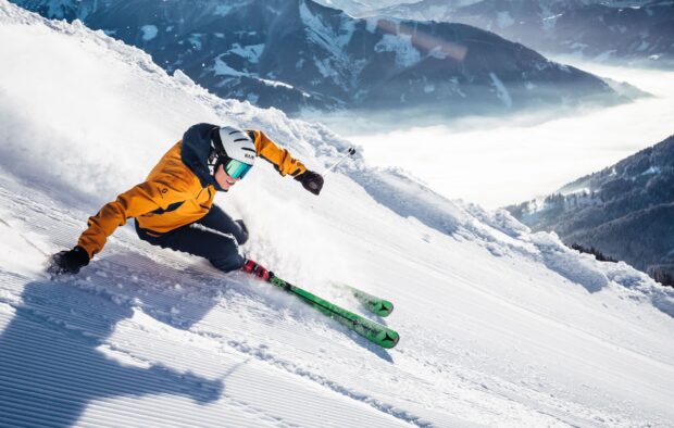A skier in a yellow jacket is performing alpine skiing on a snowy mountain slope