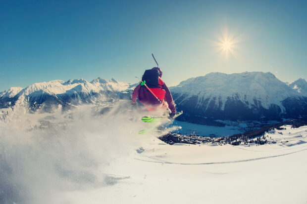 A skier wearing red gear performs alpine skiing on fresh snow with mountains in the background