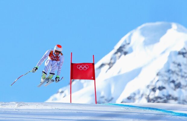 Alpine skiing athlete jumping over snow near Olympic gate