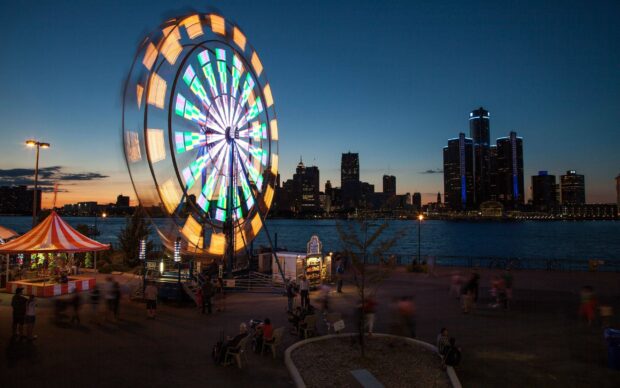 A colorful amusement park ferris wheel spinning at dusk near a city skyline